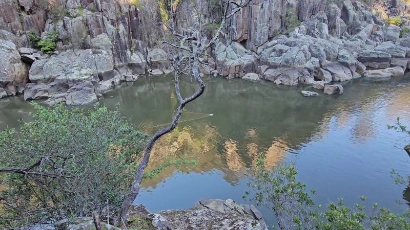 A gorge at the end of the street β A white duck on the still water of the gorge below a rock face, a thin wake trai (poster)