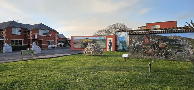 Weindorfer's mountain — More murals on low walls behind a lawn, each with a small plaque on a post in fr