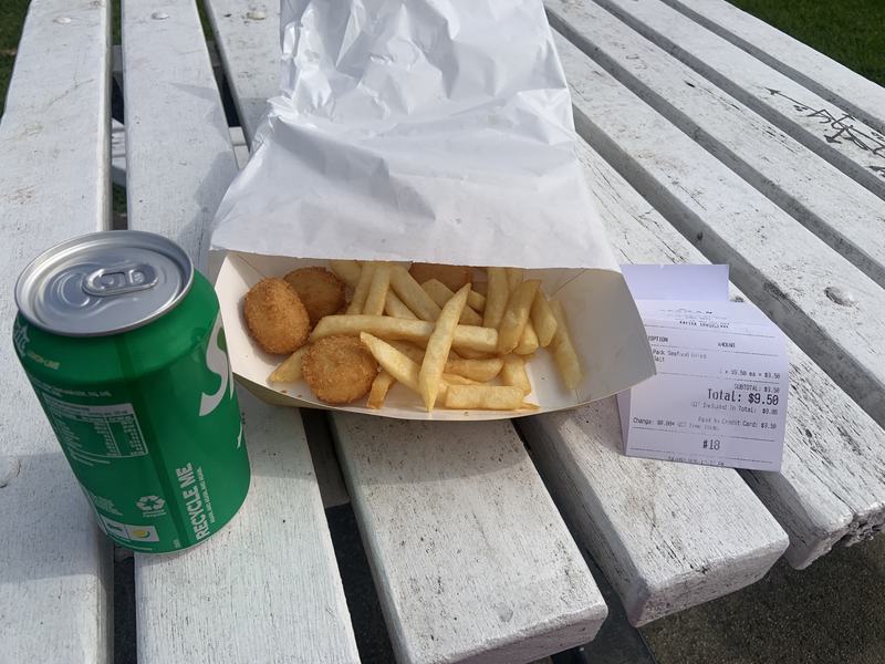 Up the Tamar — A paper tray of seafood bites and chips on a white bench, a can of Sprite and th