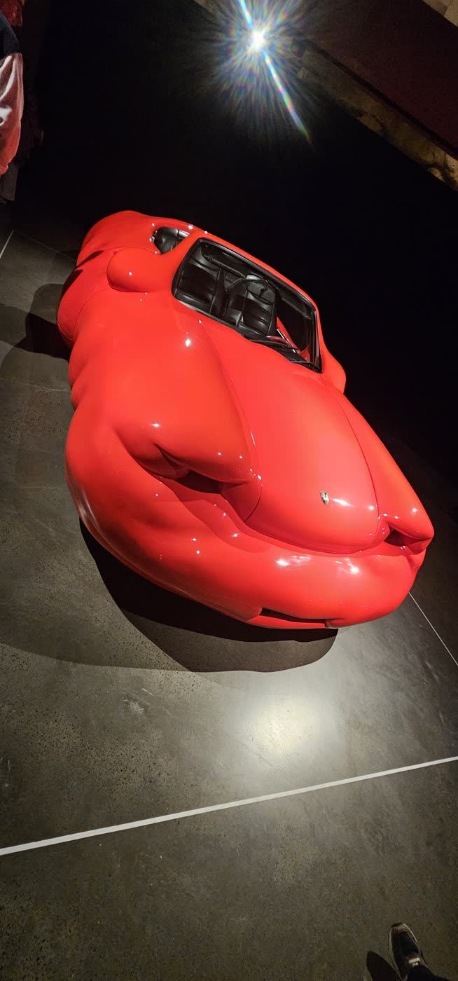 Cut into the cliff β A red Porsche swollen into soft, fleshy rolls, under a spotlight