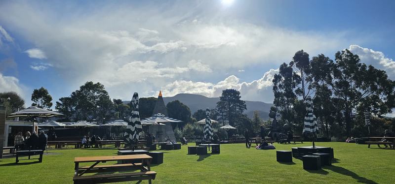 Cut into the cliff β MONA's lawn: black-and-white striped umbrellas, picnic tables and a pointed pyra