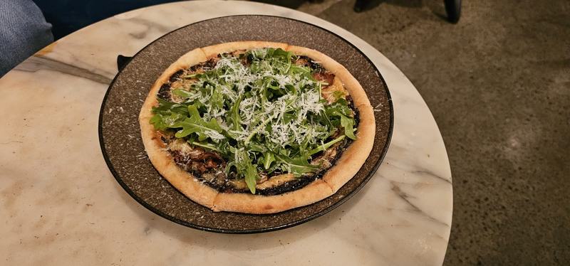 Cut into the cliff β A pizza topped with rocket and grated parmesan on a dark plate, on a marble tabl