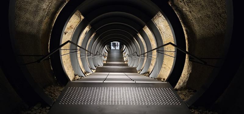 Cut into the cliff — A tunnel of steel rings cut through the sandstone at MONA, stairs running down i