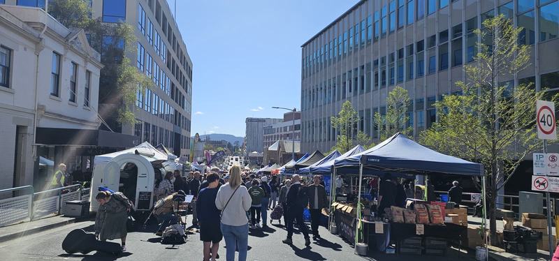 The city that faces south — Farm Gate Market: stalls under blue gazebos filling Bathurst St, crowds in the s