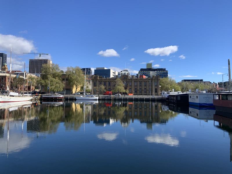 A mountain with four names — Mirror-still water in a dock, moored boats, a big sandstone building with a smal