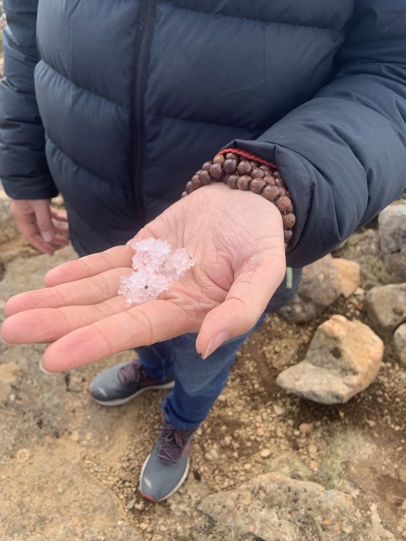 A mountain with four names — A hand in a puffer jacket sleeve holding a small handful of icy snow above rocky