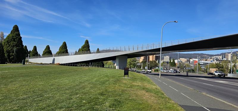 Hobart anytime — a base, not a checklist — A long, slim pedestrian bridge sweeping over a highway beside a lawn with dark c