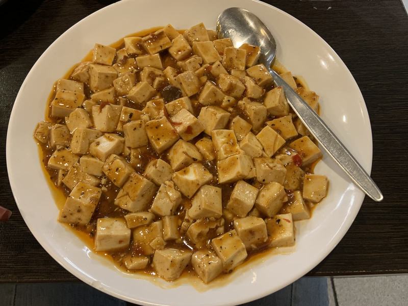 Melbourne anytime — a base, not a checklist — A white bowl of mapo tofu, cubes of tofu in a red chilli sauce, a spoon at the s