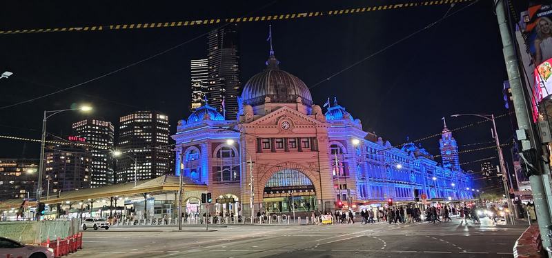 Melbourne anytime — a base, not a checklist — Flinders Street Station at night, its dome and clock tower lit blue, a crowd cro