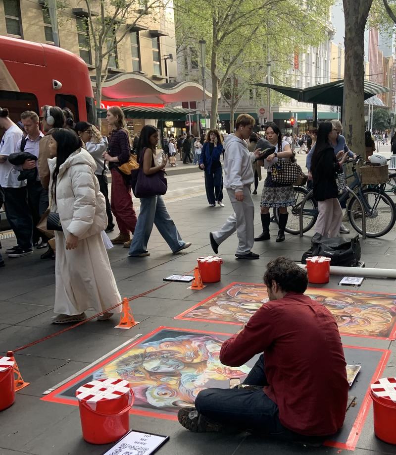 Melbourne anytime — a base, not a checklist — A pavement artist in a red shirt kneeling over a colourful chalk-pastel portrait