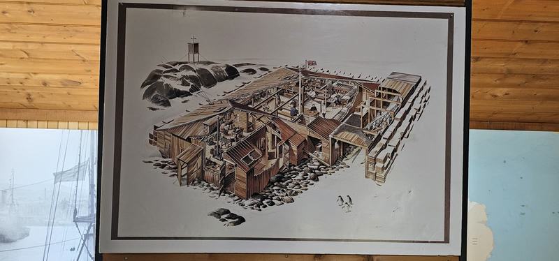 The city that faces south — A framed cutaway drawing of the Cape Denison huts banked with snow, men at the t