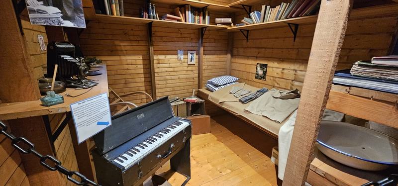 The city that faces south — Mawson's room in the replica: a narrow bunk with folded clothes, a bookshelf, a