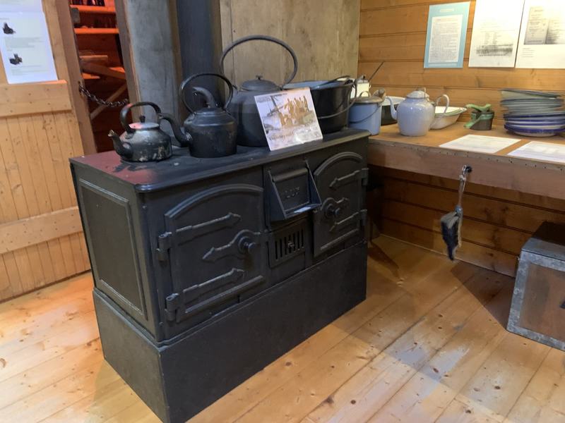The city that faces south — A black iron stove with kettles and pots on top, an enamel-ware bench and plates