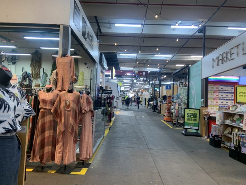 What the gold paid for — A market aisle with linen dresses on mannequins at the left, string lights overh