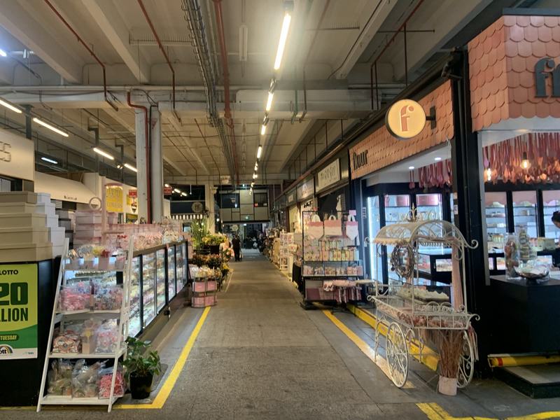 What the gold paid for — A covered market aisle with yellow floor lines, glass cases of cakes and sweets