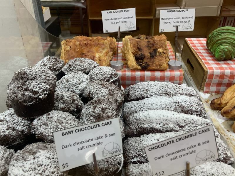 What the gold paid for — A pastry counter with two puff pastries and rows of dark chocolate cakes dusted
