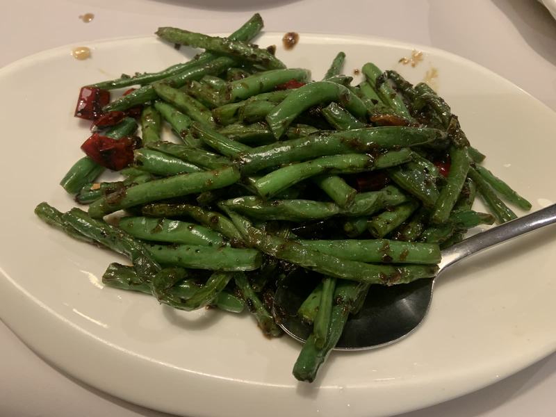What the gold paid for — A white oval plate of dry-fried green beans with dried red chillies, a serving s