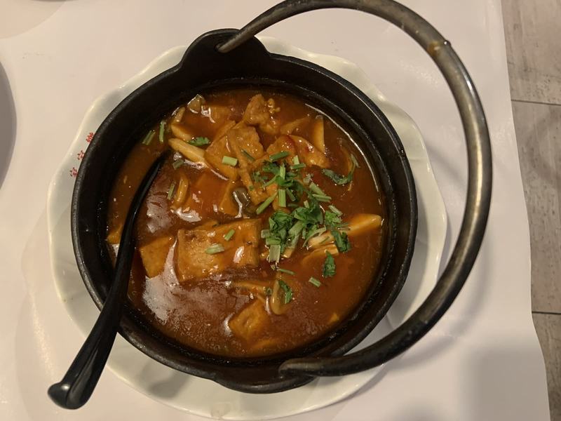 What the gold paid for — Braised tofu and mushrooms in a red-brown sauce in a black iron pot with a handl