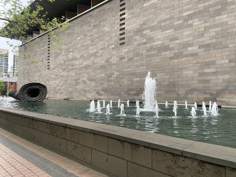 What the gold paid for — A long pool of fountains in front of the NGV's high stone wall, a coiled black s