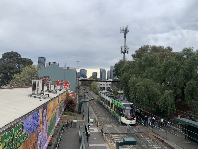 What the gold paid for — A green-and-white tram stopped at a platform in a leafy cutting, passengers walk