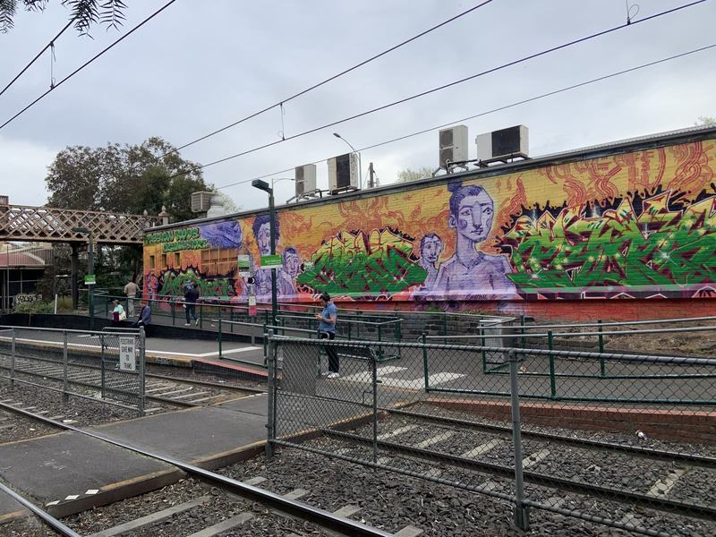 What the gold paid for — A colourful mural of purple faces and green lettering across a brick wall behind